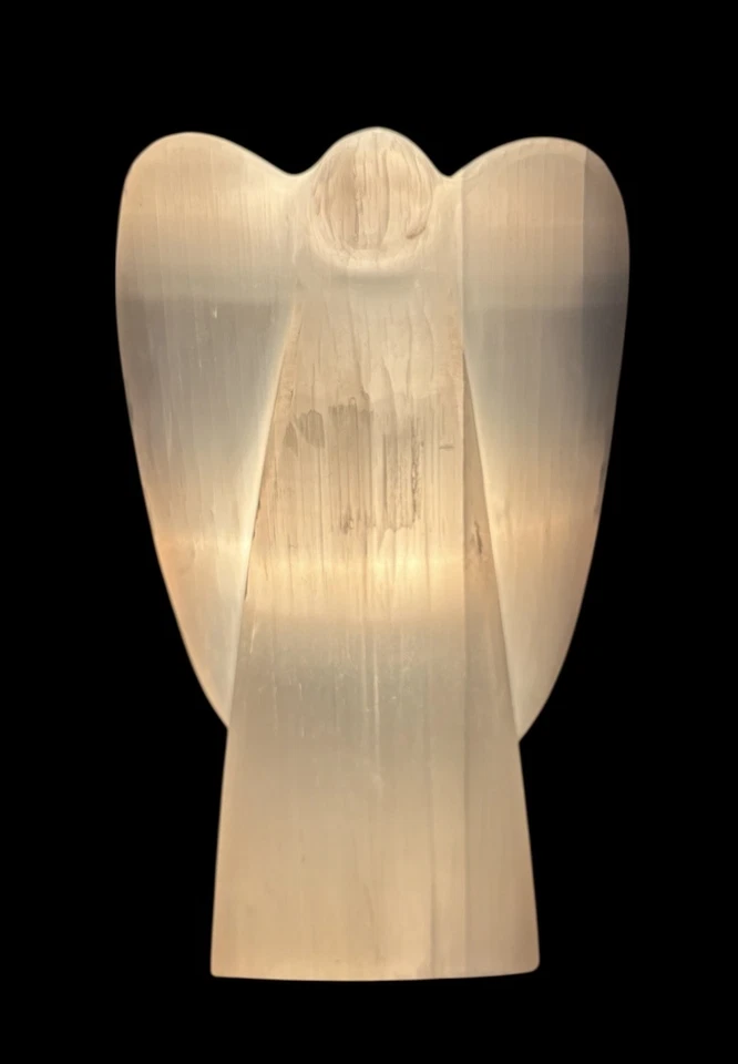 Natural selenite angel lamp illuminated with warm light on a black background
