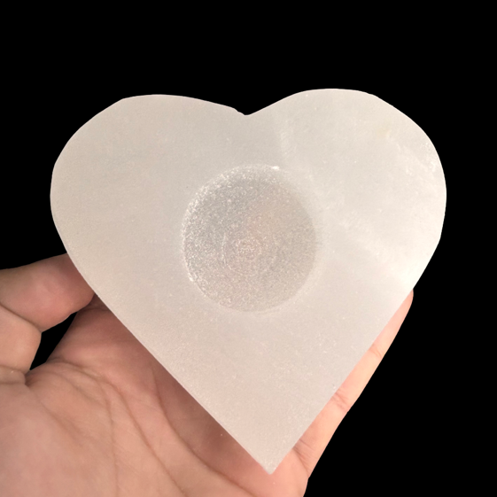 Heart shaped polished natural selenite candle holder displayed in hand for size reference