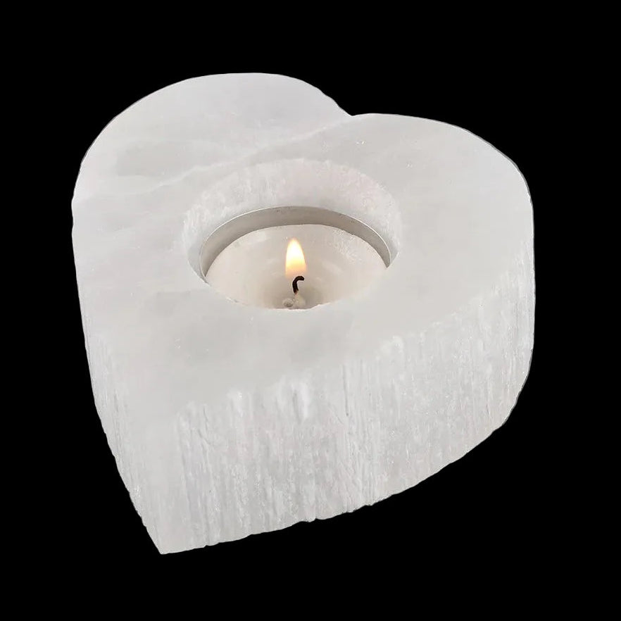Lit tealight inside heart shaped natural selenite candle holder with polished surface and Moroccan crystal texture