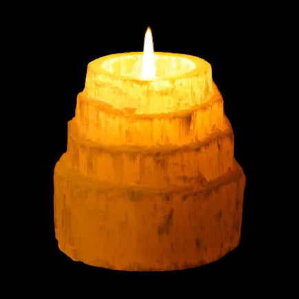 Lit tealight inside natural selenite candle holder creating warm ambient glow on black background